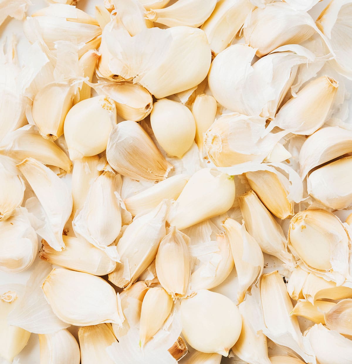 A close up view detailing the texture of a large pile of unpeeled garlic cloves