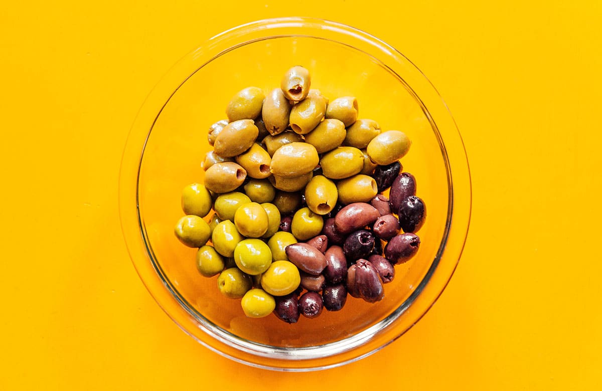 A clear glass bowl filled with mixed olives