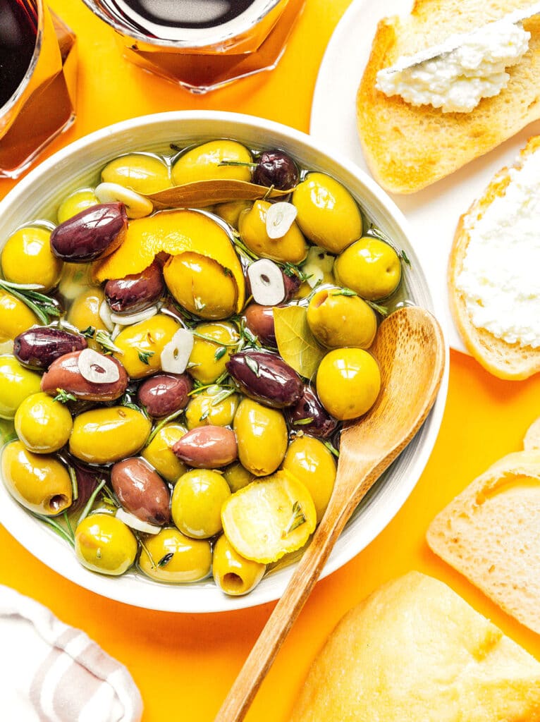 A white bowl filled with marinated olives with a wooden spoon dipped inside