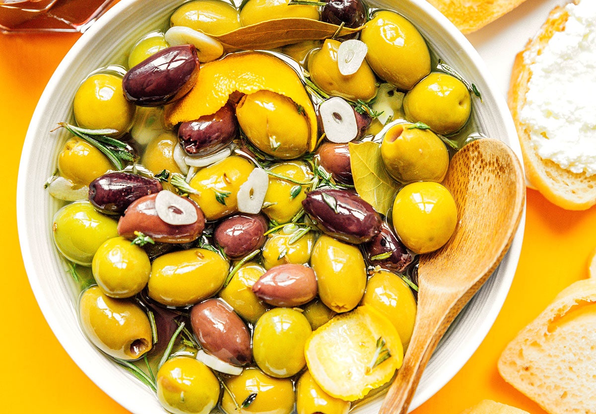 A white bowl filled with Mediterranean marinated olives with a wooden spoon dipped inside