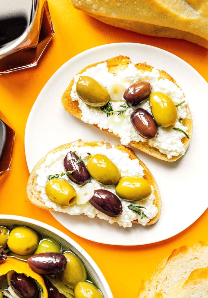 Two slices of bread topped with a spread and marinated olives