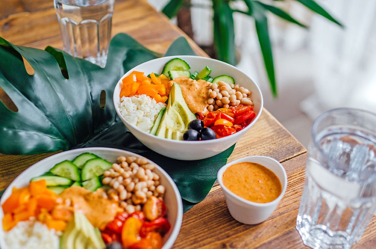A Mediterranean romesco bowl made with grated cauliflower, diced bell pepper, roasted tomatoes, sliced avocado, sliced cucumber, white beans, and black olives