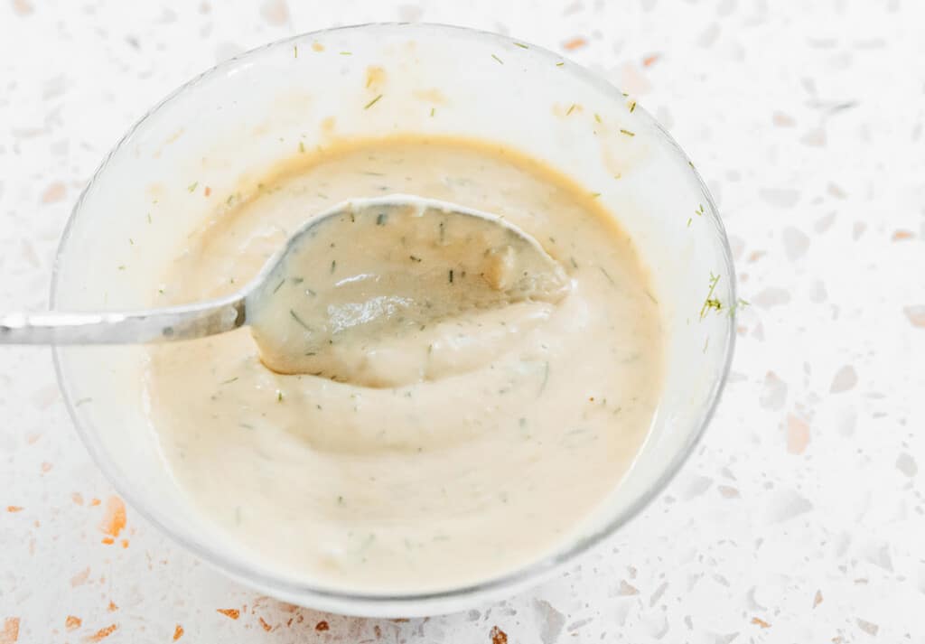 Dill hummus dressing in a bowl with a spoon.