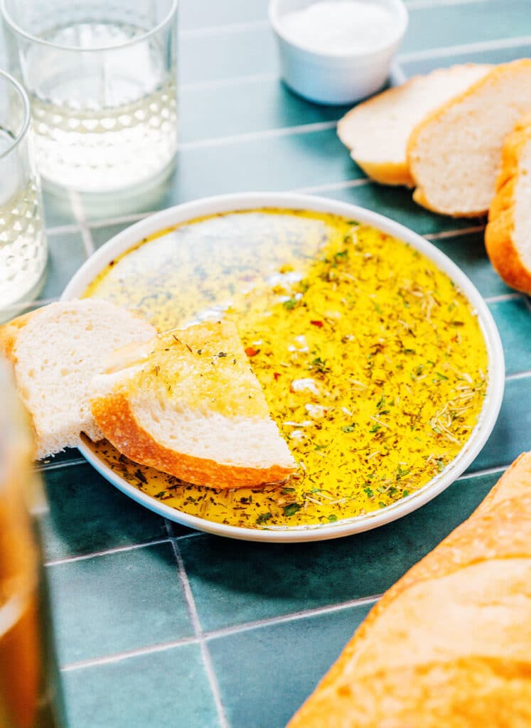 A while bowl filled with olive oil bread dip with 2 slices of bread resting inside