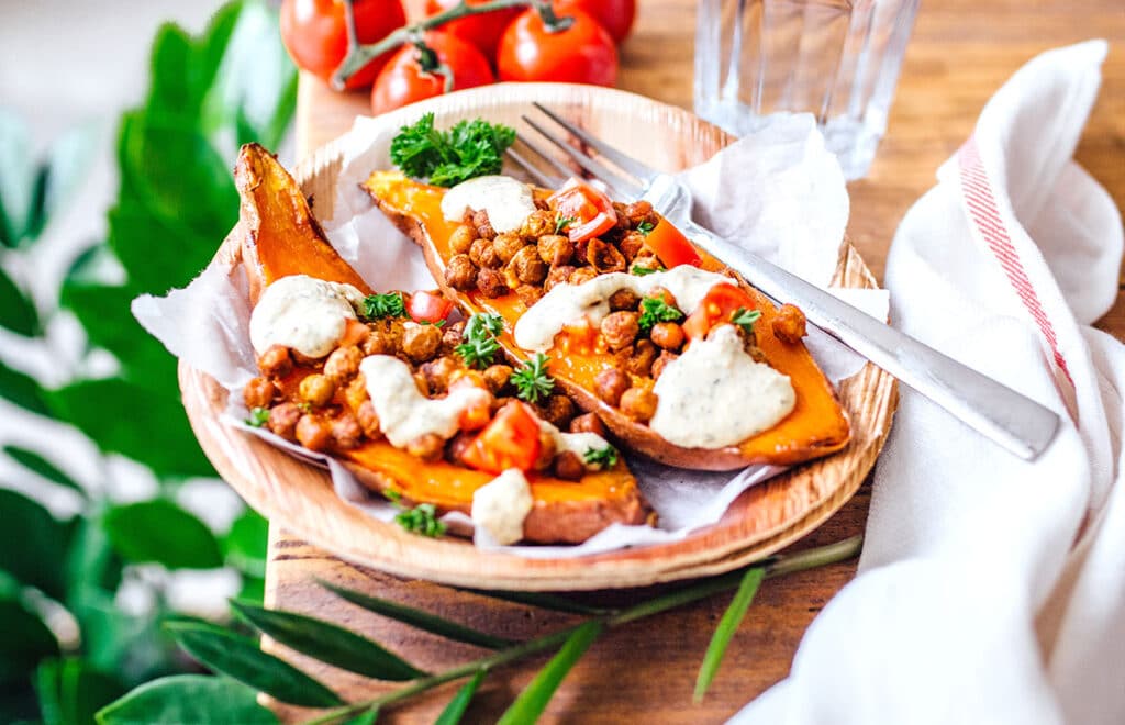 A wooden bowl with two Mediterranean stuffed sweet potatoes inside resting atop a piece of parchment paper 