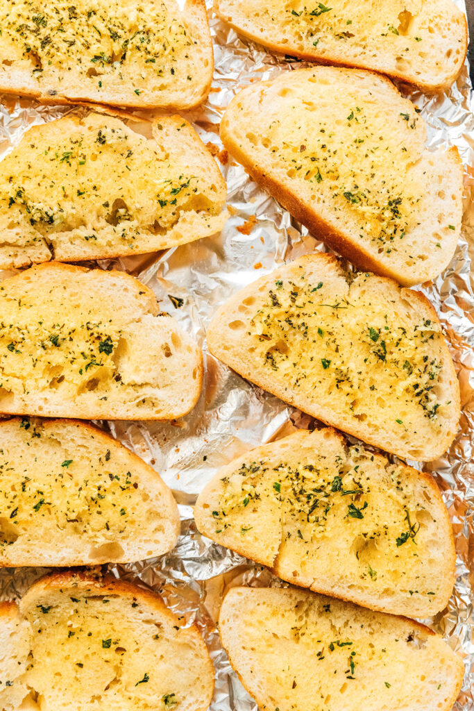 Ten slices of garlic bread lined up on a piece of aluminum foil