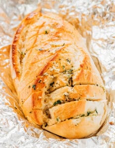 Sliced vegan garlic bread wrapped in foil, topped with herbs and plant-based butter.