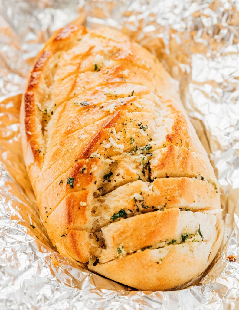 A large loaf of garlic bread placed on a sheet of aluminum foil