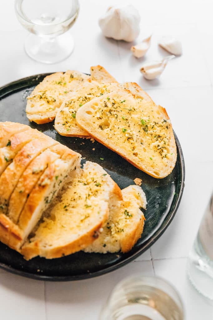 A black plate filled with a loaf and slices of vegan garlic bread