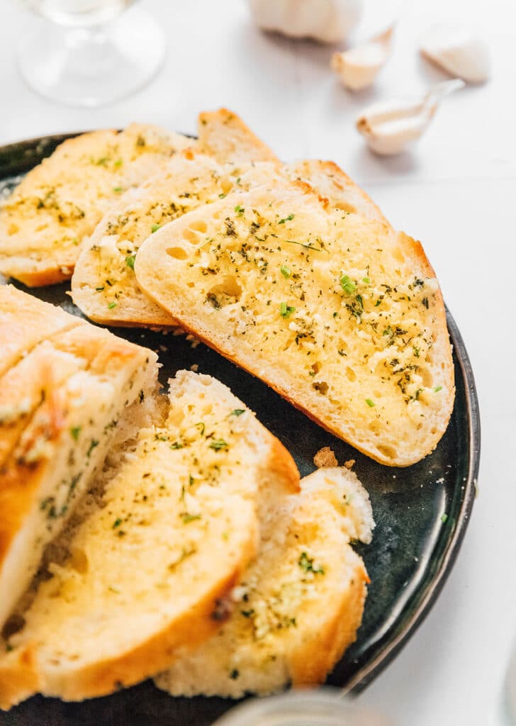 A black plate filled with a loaf and slices of garlic bread