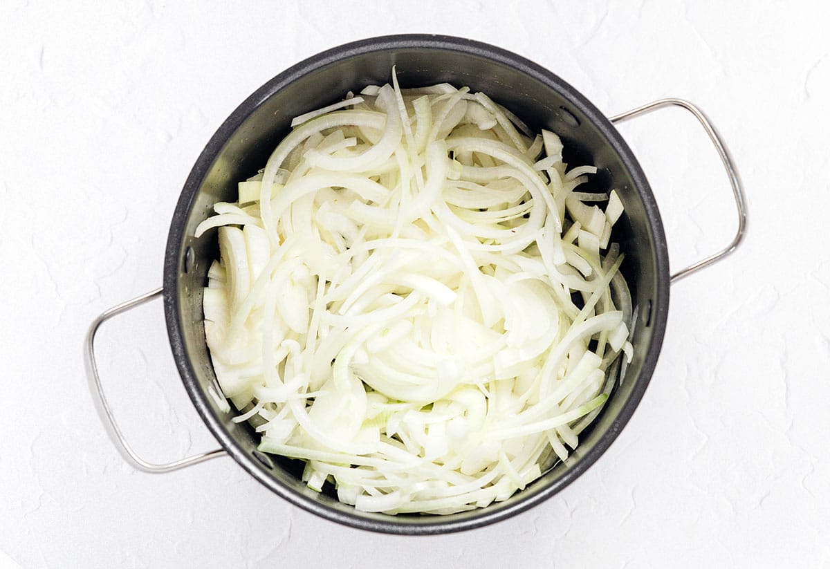 A large pot filled with uncooked sliced white onion