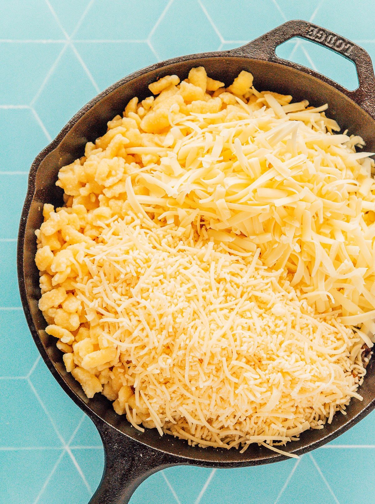 A cast iron skillet filled with caramelized onions, spaetzle, and shredded cheese