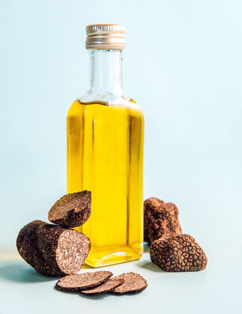 A jar of olive oil with whole and shaved black truffles scattered around