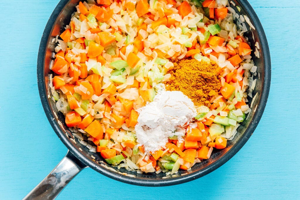 A pot filled with cooked carrots, celery, white onion, and various spices