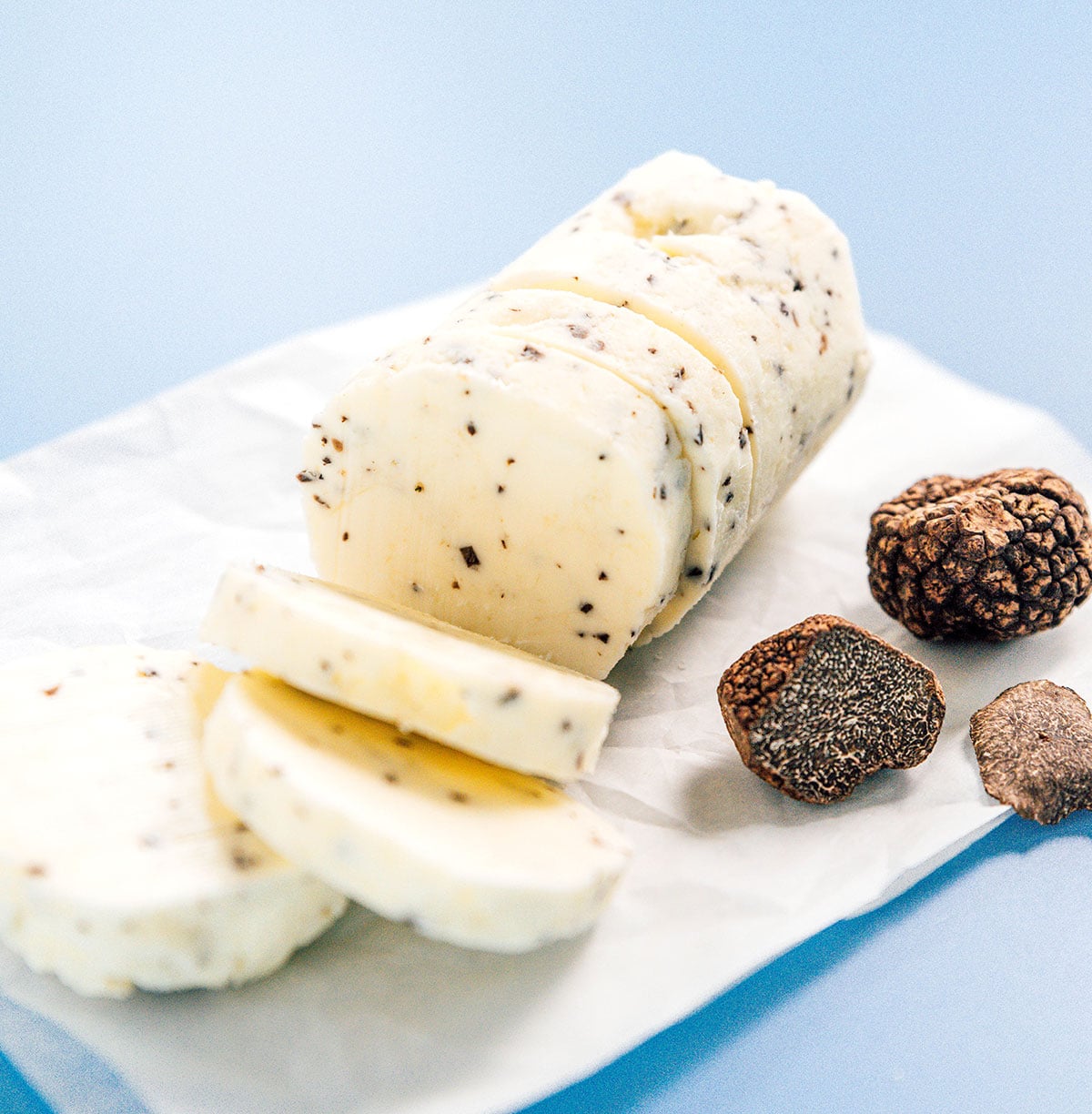 A log of black truffle butter sitting on top of a piece of parchment paper beside a couple of black truffles