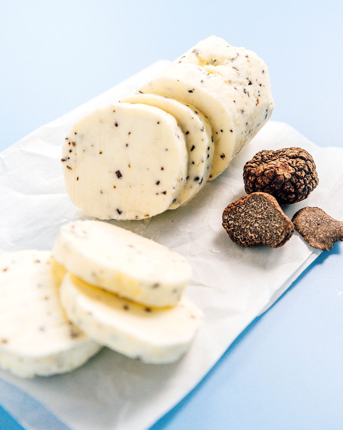 A roll of truffle butter sitting on top of a piece of parchment paper beside a couple of black truffles