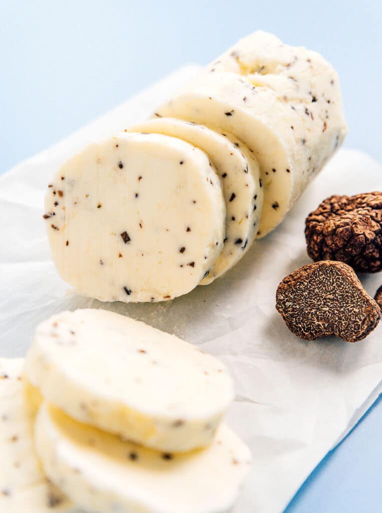 Black truffle butter sitting on top of a piece of parchment paper with a couple of black truffles