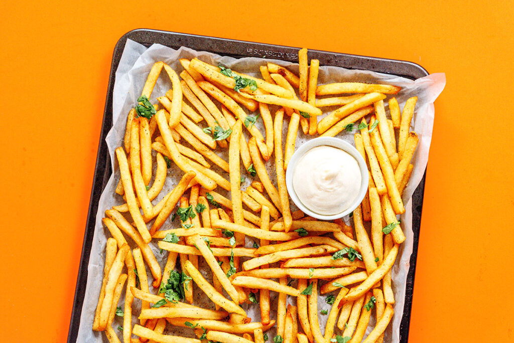 A baking sheet filled with garnished truffle fries paired with a small bowl of white dipping sauce
