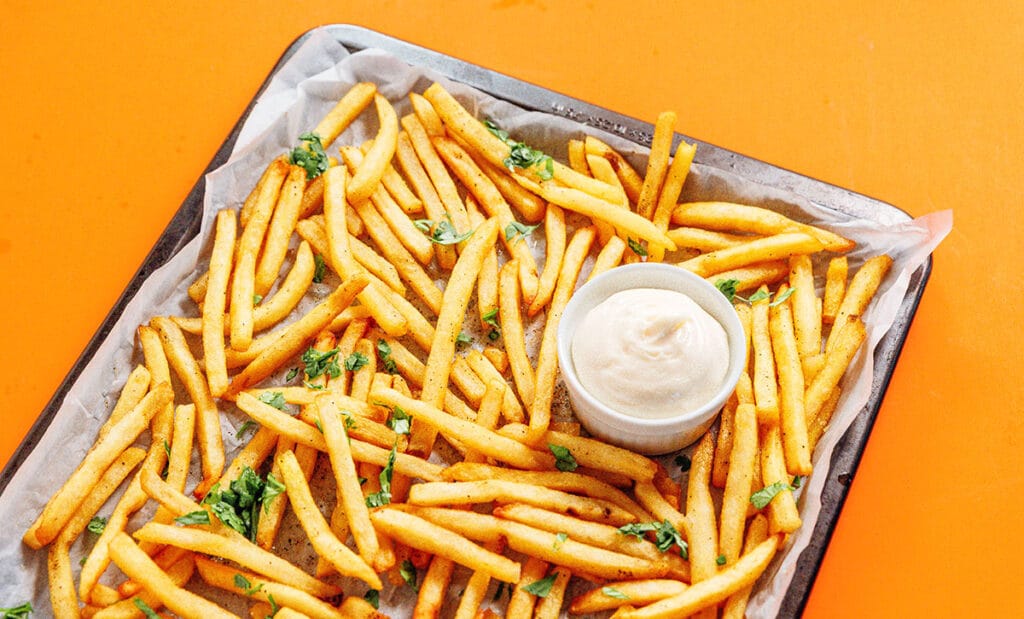 A baking sheet filled with cooked and garnished truffle fries and a small container of dipping sauce