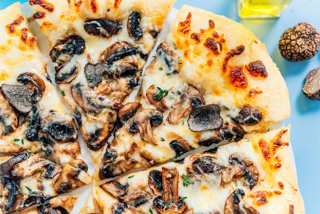 A bird's eye view of truffle mushroom pizza with truffle oil and whole truffles off to the side