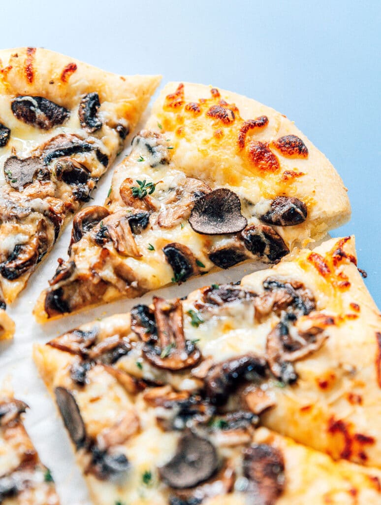 Slices of black truffle pizza topped with mushrooms, herbs, and black truffle