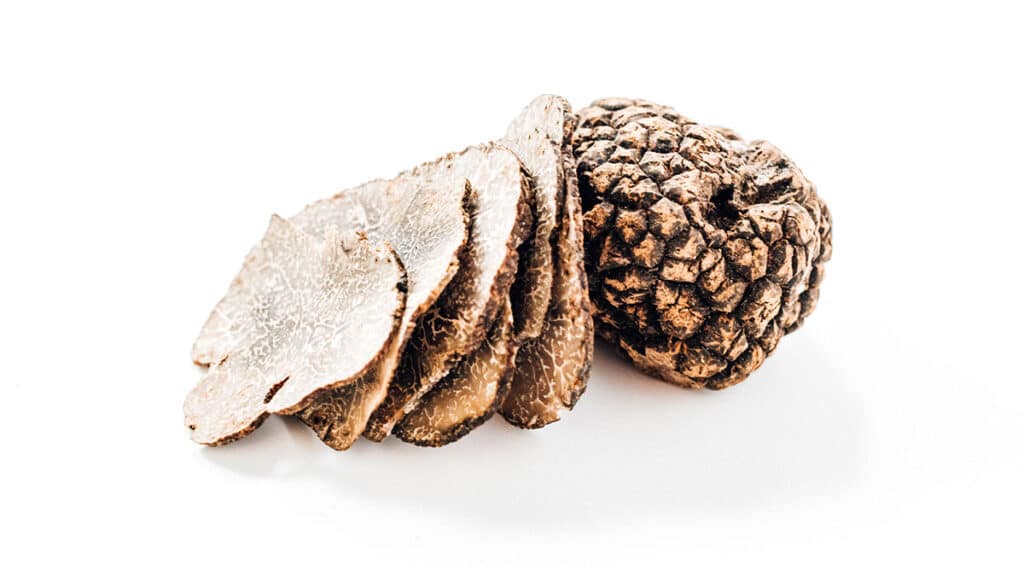 Five slices of a truffle mushroom next to a whole truffle