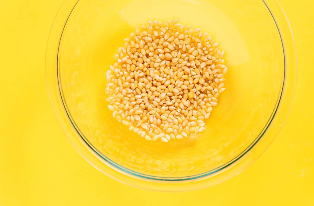 A clear glass bowl filled with 1/2 cup of unpopped popcorn kernels