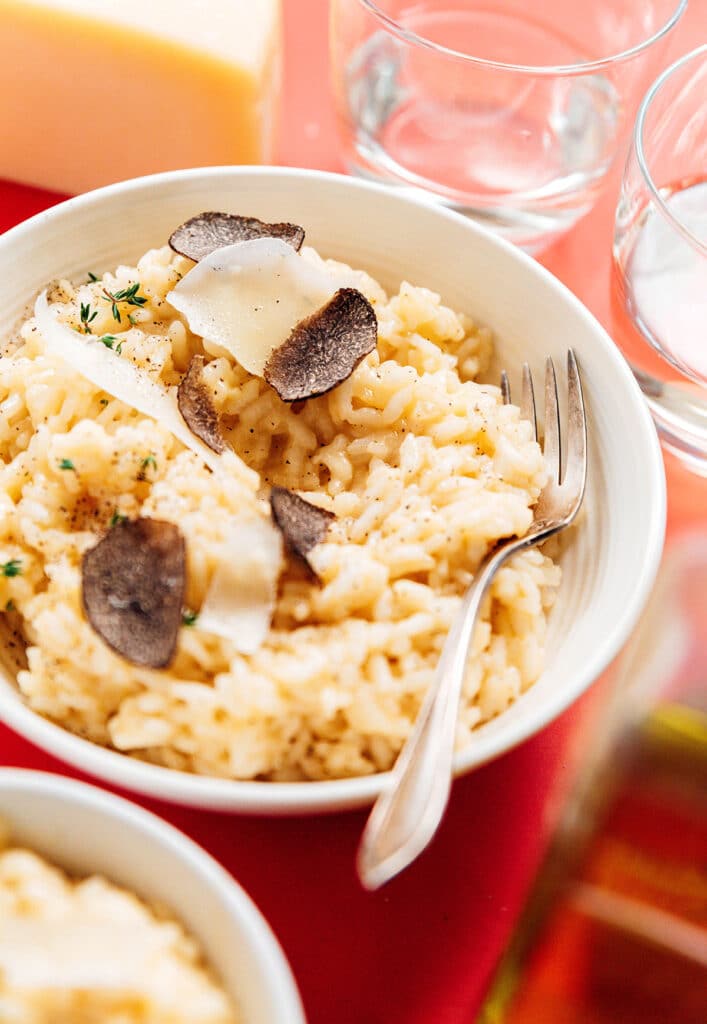 A white ceramic bowl filled with fresh truffle risotto garnished with parmesan cheese, truffles, and herbs