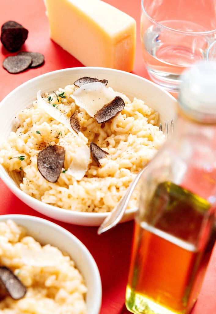 A white ceramic bowl filled with parmesan truffle risotto garnished with parmesan cheese, truffles, and herbs