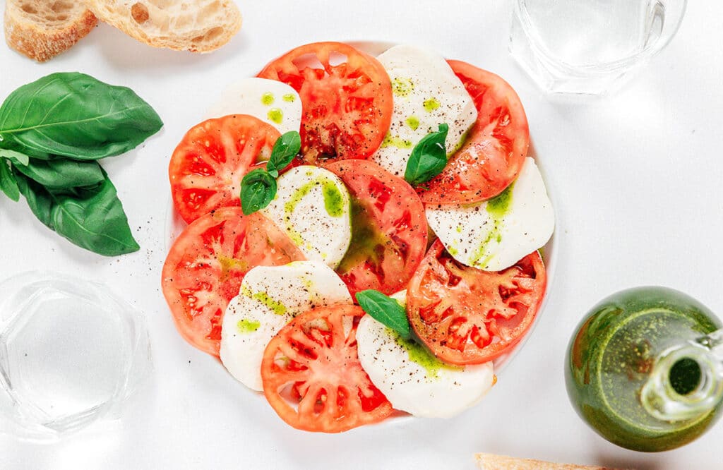 A plate of tomato and mozzarella slices garnished with basil and basil oil