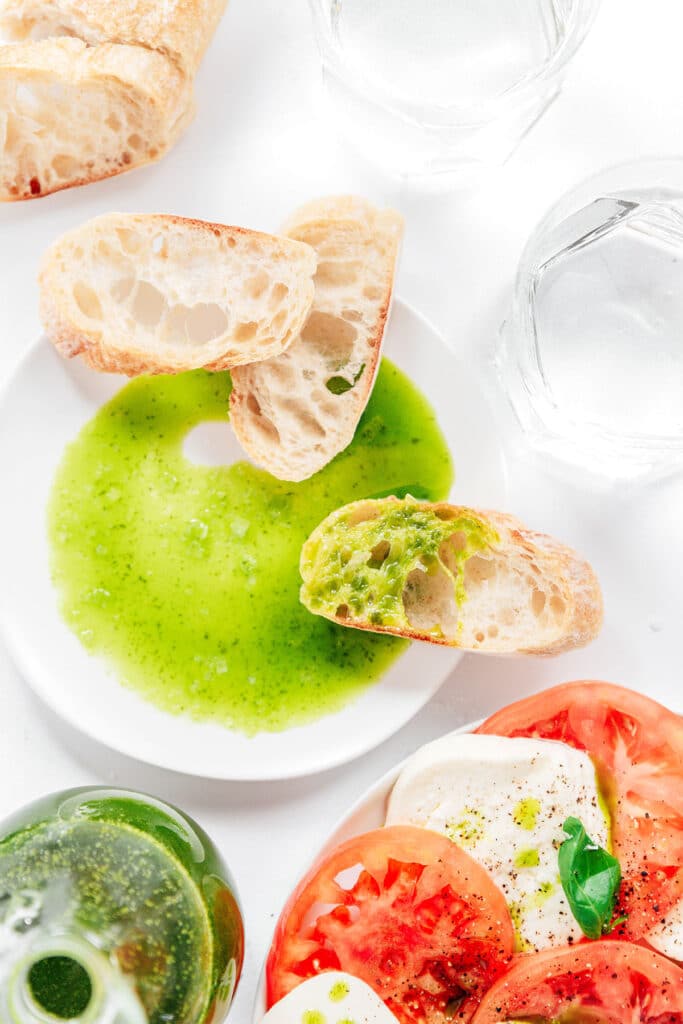 A shallow white dish filled with herb oil with a few slices of bread resting on the edges of the dish