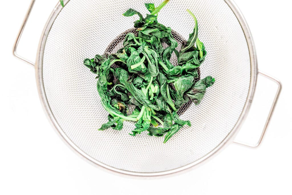 A strainer filled with cooked basil leaves
