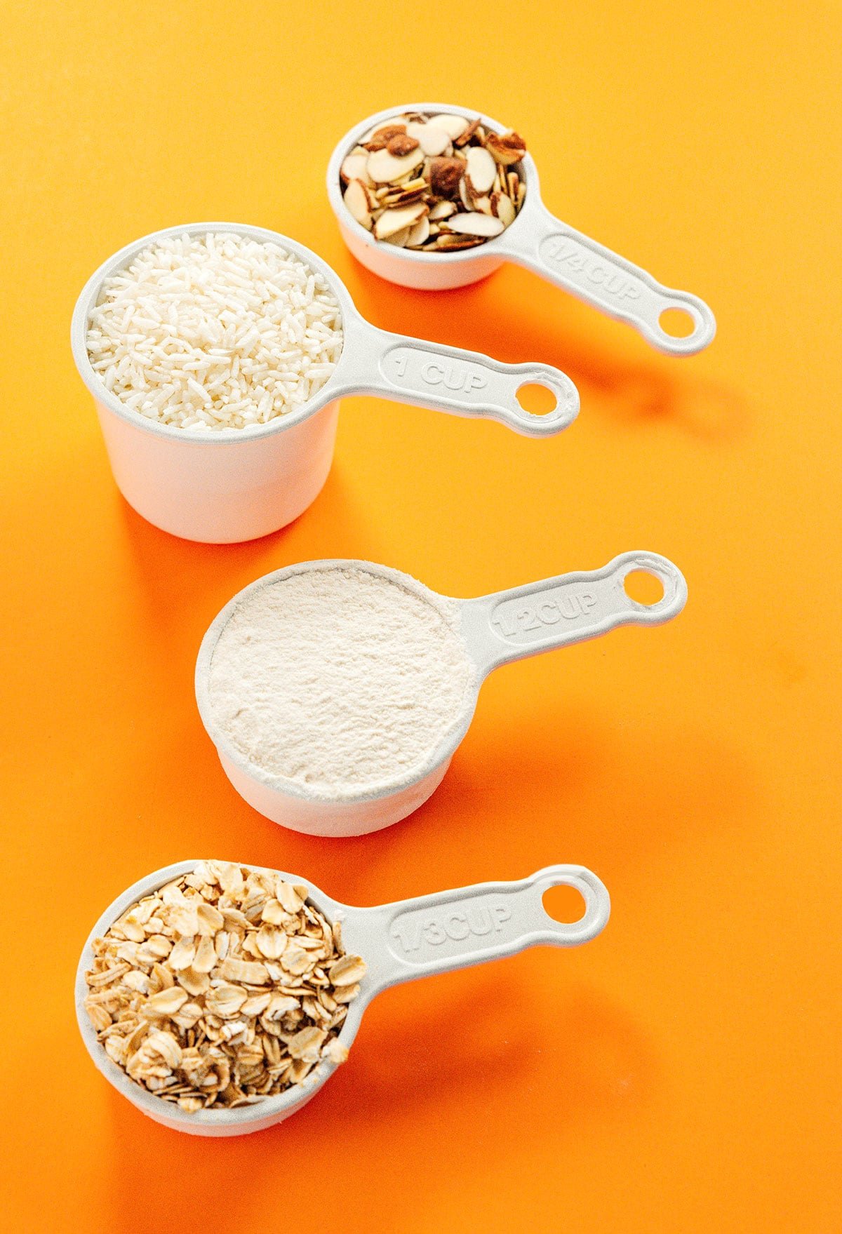 Solid measuring cups with oats, flour, and rice in them.