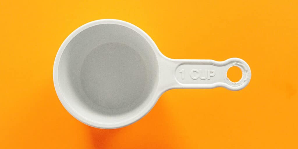 An empty white plastic one-cup measure on an orange surface.