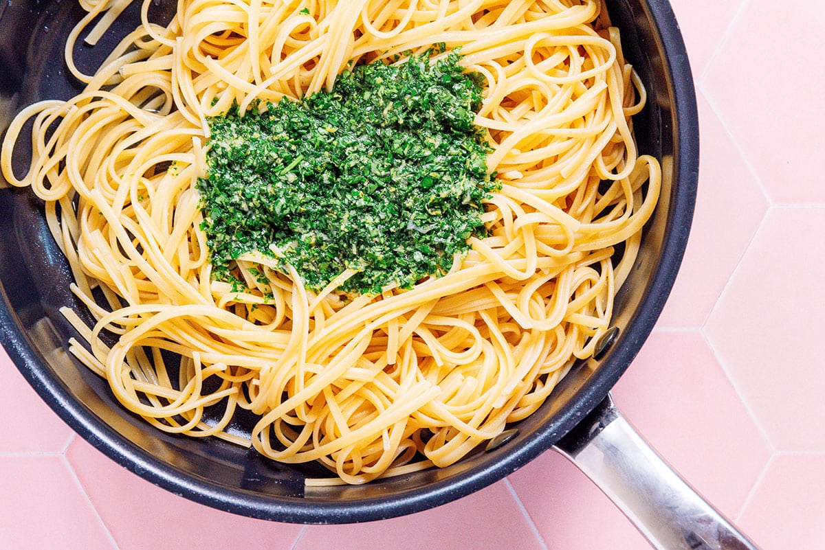 A pot filled with linguini with a pile of gremolata on top