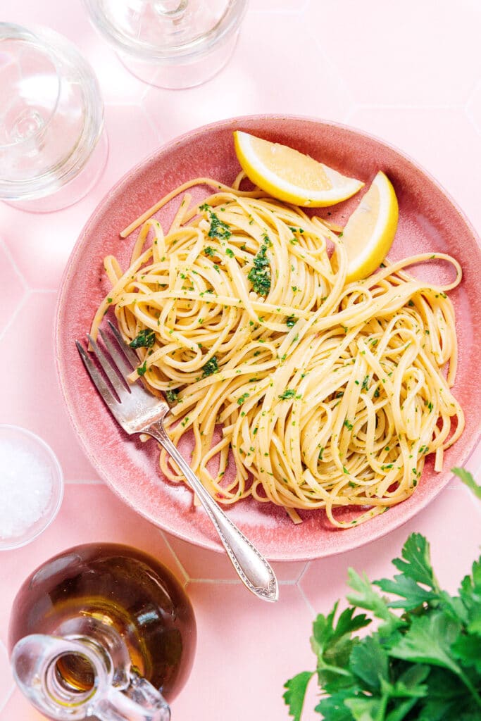 A pink bowl filled with gremolata pasta and two lemon wedges
