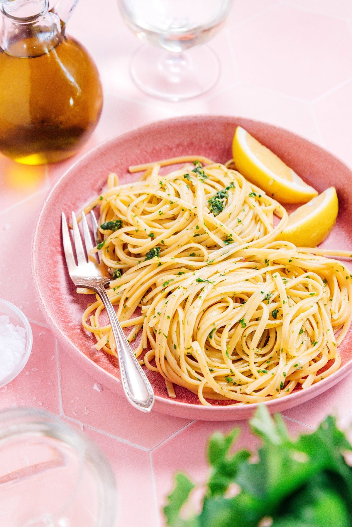 A shallow pink bowl filled with Mediterranean pasta and two lemon wedges