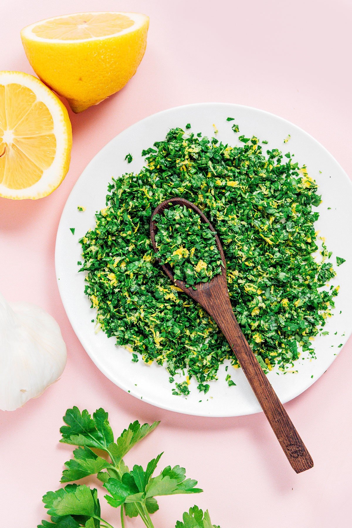 A white bowl filled with gremolata with a wooden spoon resting inside