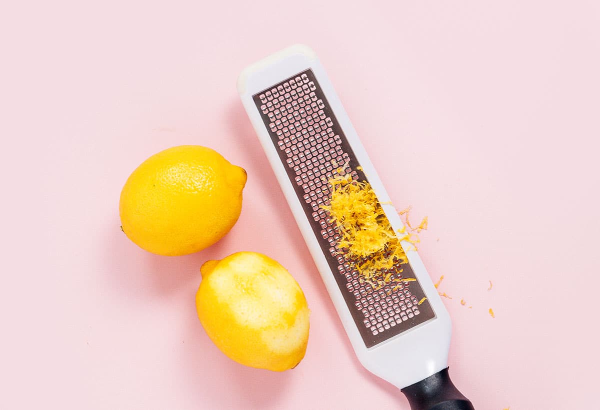 Two lemons beside a grater with lemon zest in the grooves