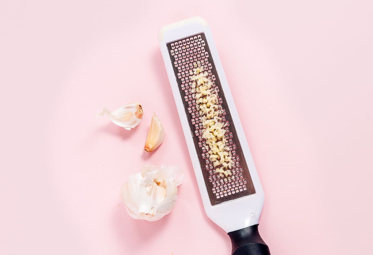 A head and clove of garlic beside a grater with garlic in the grooves