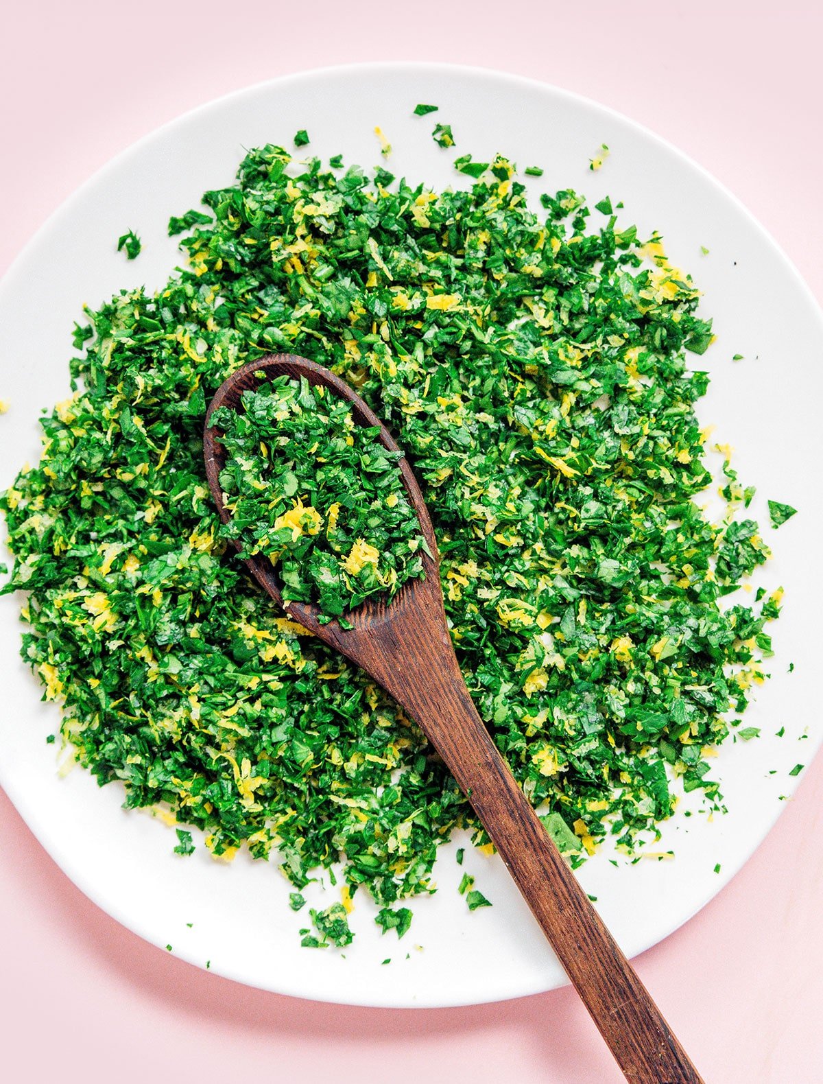 A white bowl filled with gremolata with a wooden spoon resting inside