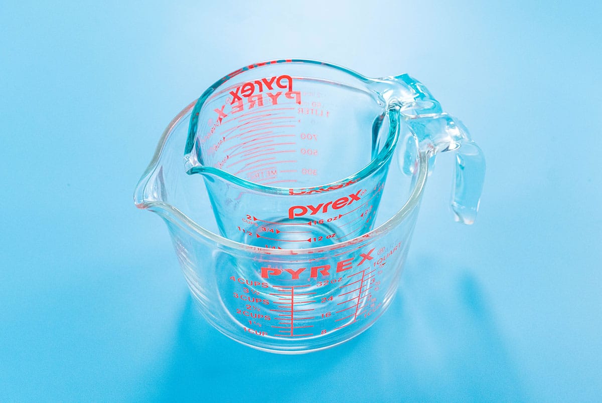 Two glass Pyrex cups stack into each other on a blue background.