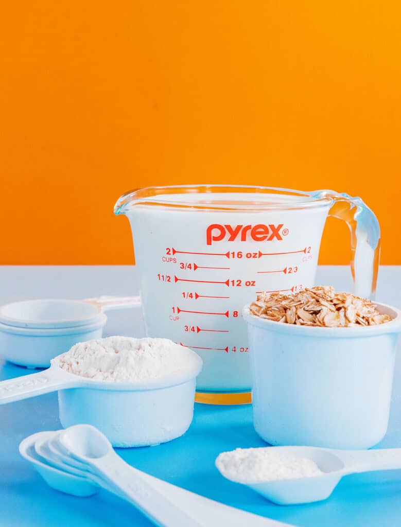 Various measuring cups filled with ounces of milk, oats, and flour