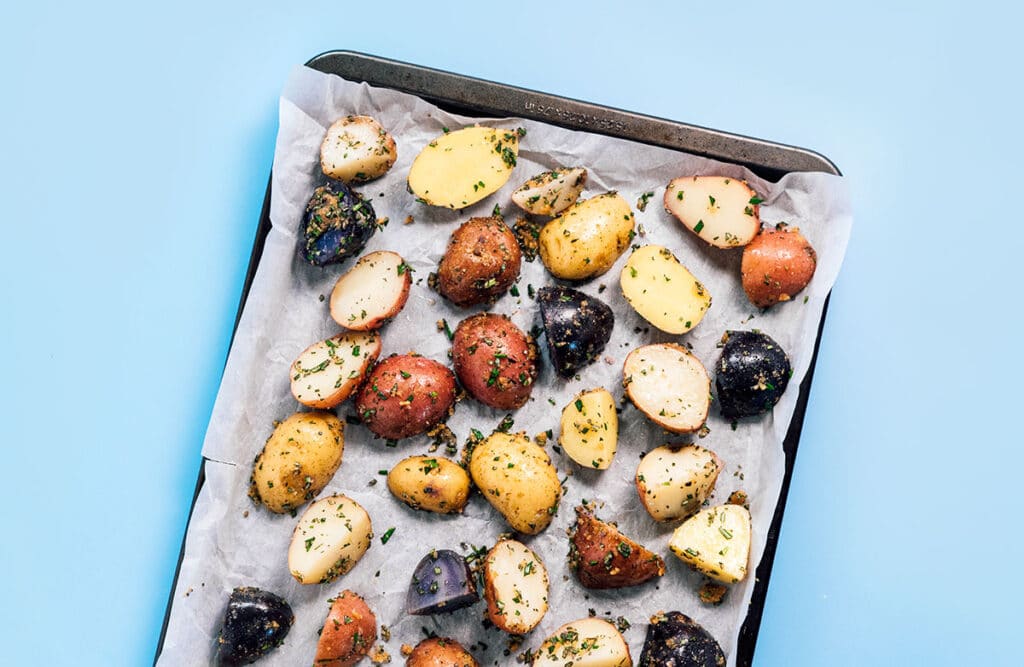 A baking sheet lined with parchment paper and topped with a single layer of uncooked rosemary potatoes