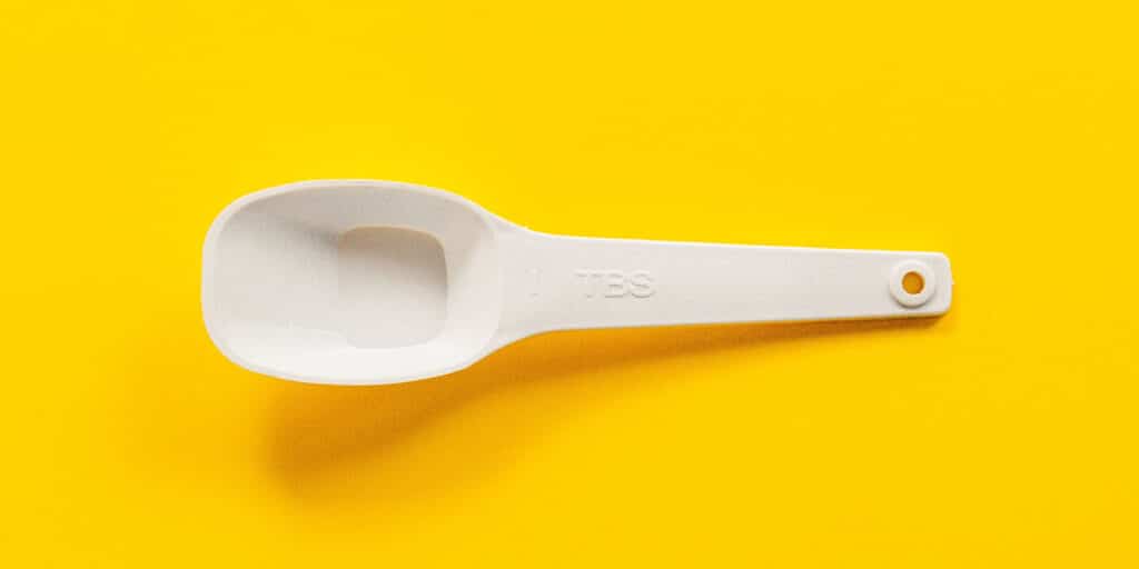 An empty white plastic tablespoon on a yellow surface.