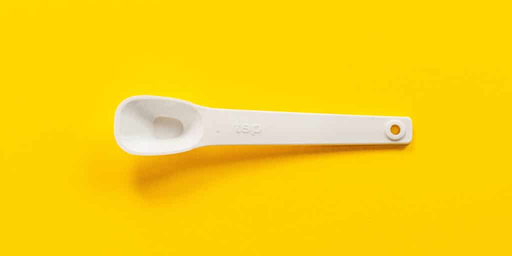A teaspoon measuring spoon on a yellow background