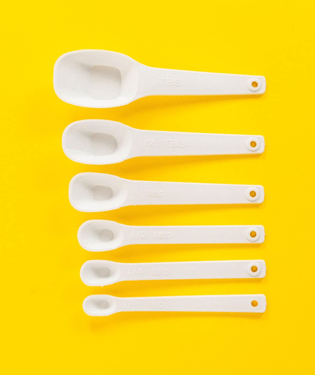 Six measuring spoons laid out on a yellow background in a row from largest to smallest