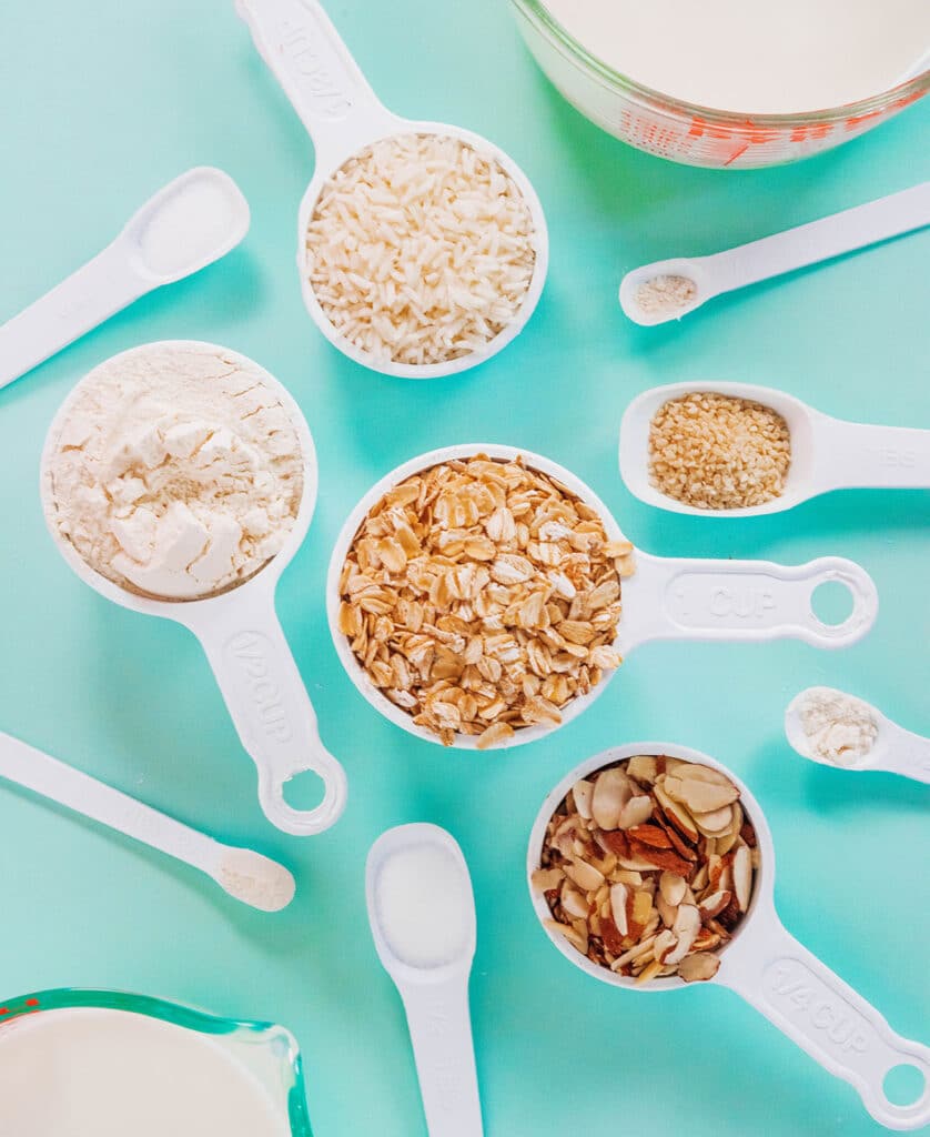 White measuring cups and spoons filled with various ingredients on a teal surface.
