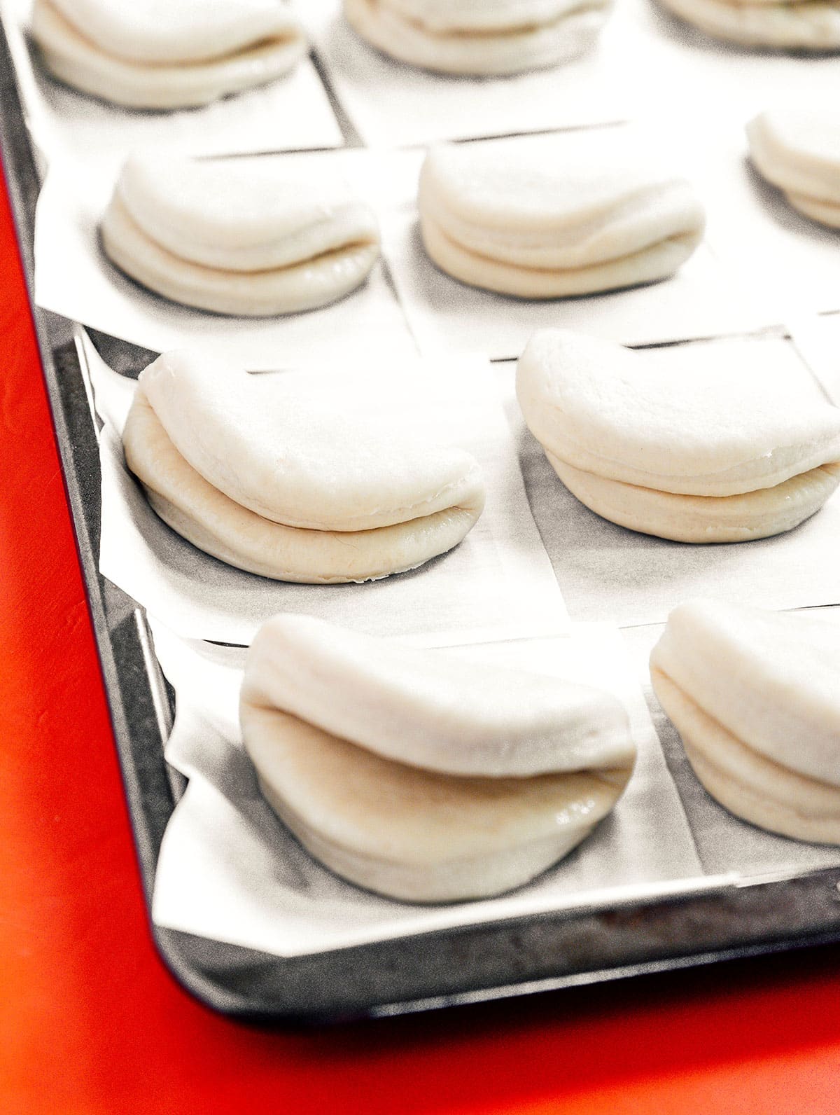 A baking sheet lined with parchment paper squares topped with uncooked bao buns