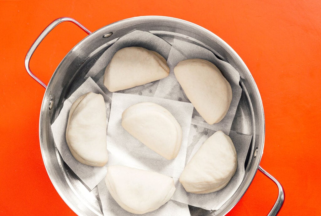 Six bao buns arranged neatly on parchment paper squares in a steamer